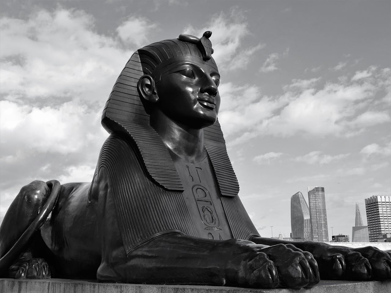 Black and white Sphinx statue located against cloudy sky near contemporary metropolitan city